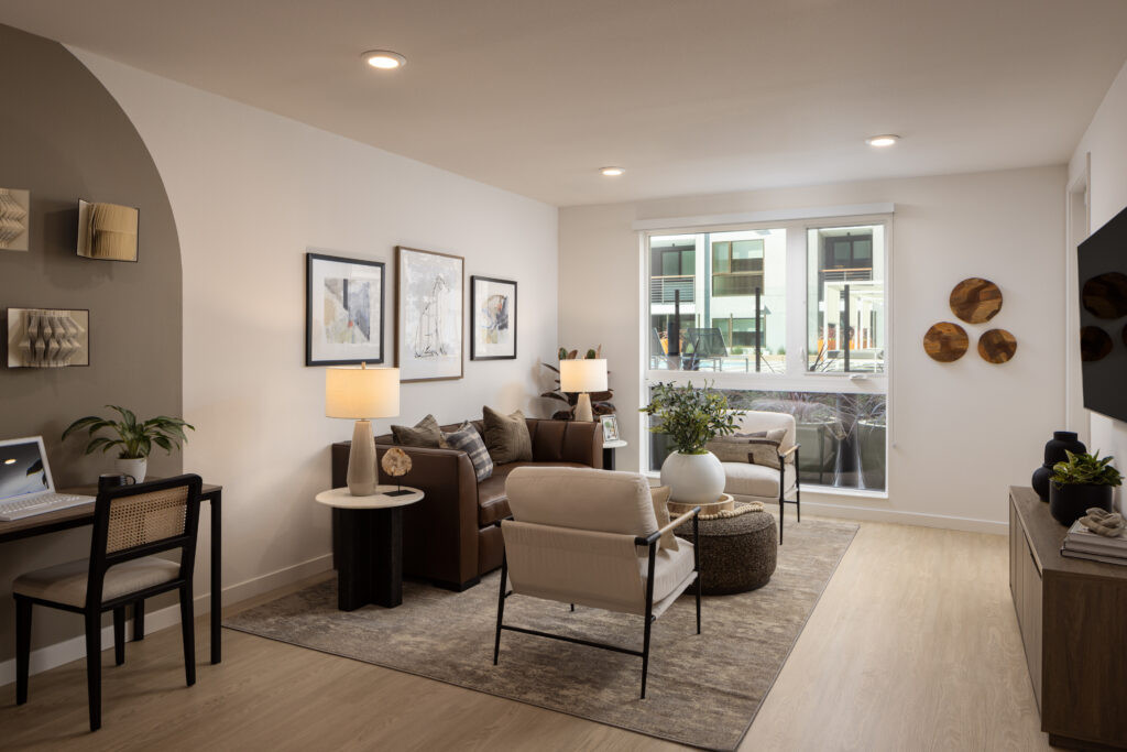 Mountain View, CA, Luxury Apartments Near Microsoft Campus - Avelle - Staged Living Room With Sofa, Accent Chairs, Home Office Desk, Large Window, And Wall Mounted Television.