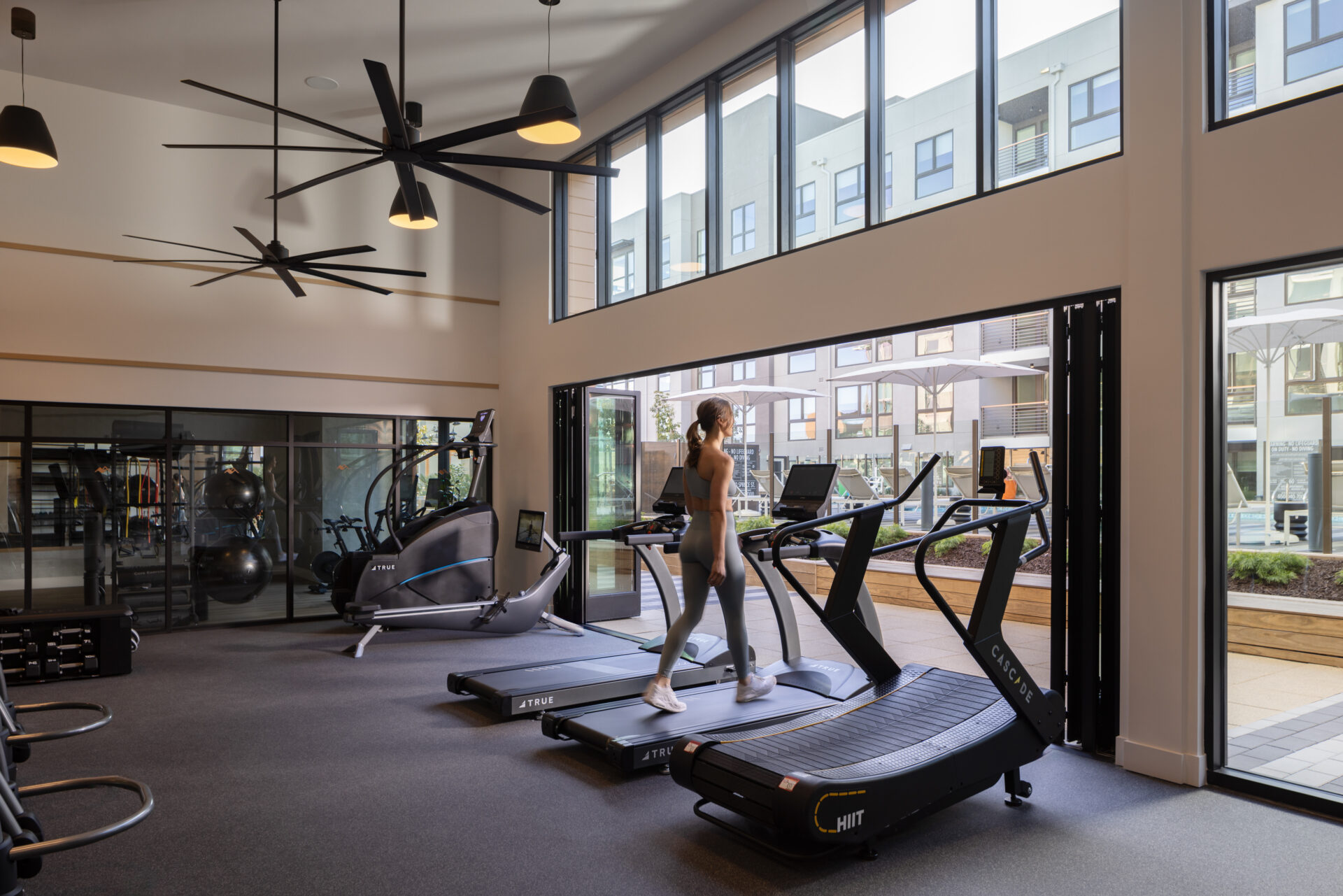 Luxury Studio Apartments Mountain View, CA - Avelle - Two Story Fitness Center With Treadmills, High Windows, Modern Pendant Lights, And Courtyard Views.