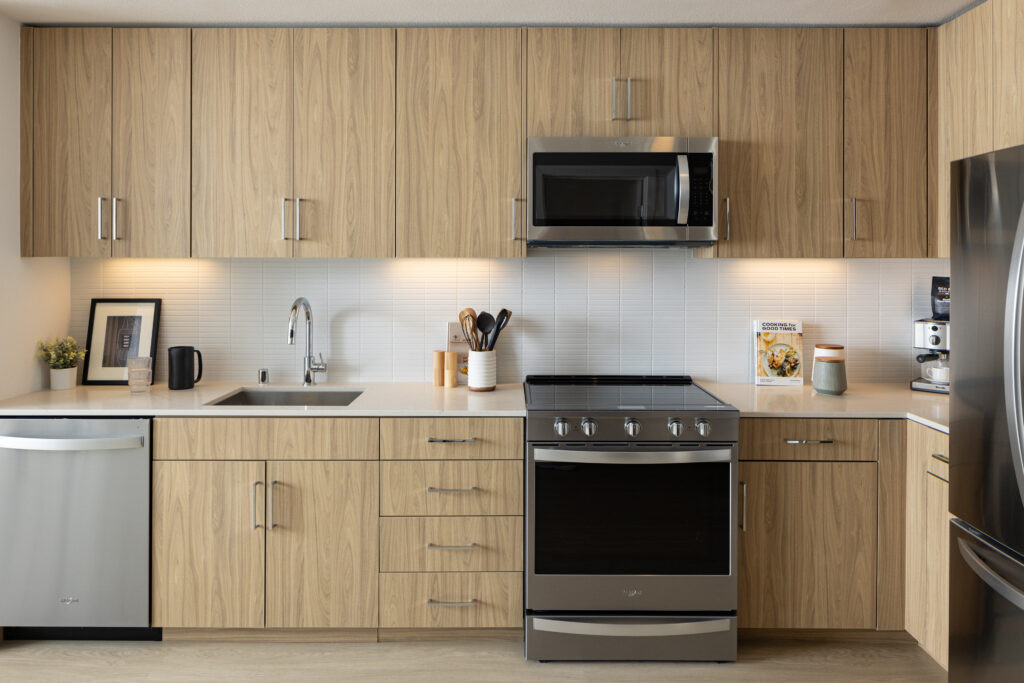 One-Bedroom Luxury Apartments in Mountain View, CA - Avelle - Modern Apartment Kitchen With Wood Cabinets, White Tile Backsplash, Quartz Counters, And Stainless Steel Appliances.