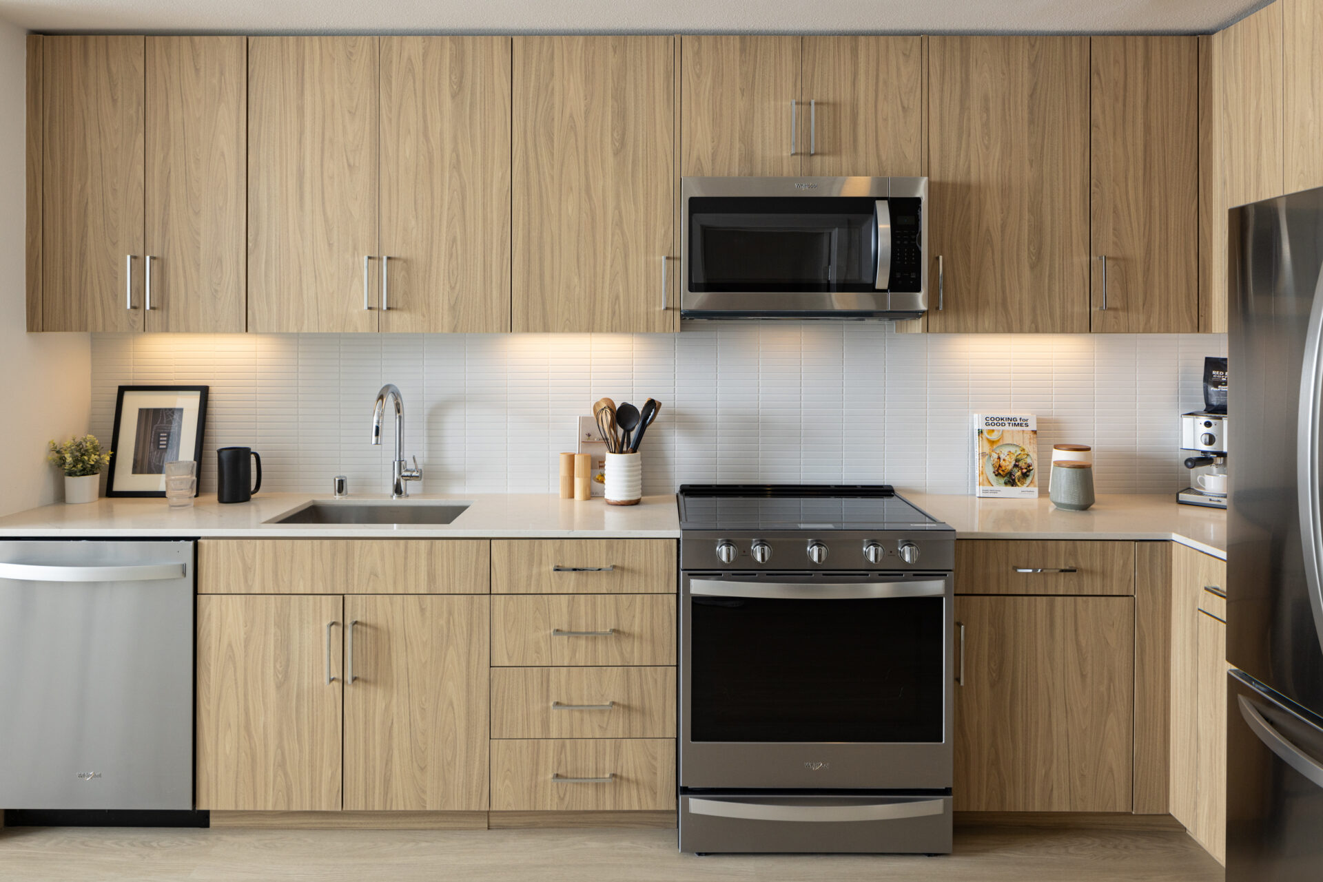 One-Bedroom Luxury Apartments in Mountain View, CA - Avelle - Modern Apartment Kitchen With Wood Cabinets, White Tile Backsplash, Quartz Counters, And Stainless Steel Appliances.